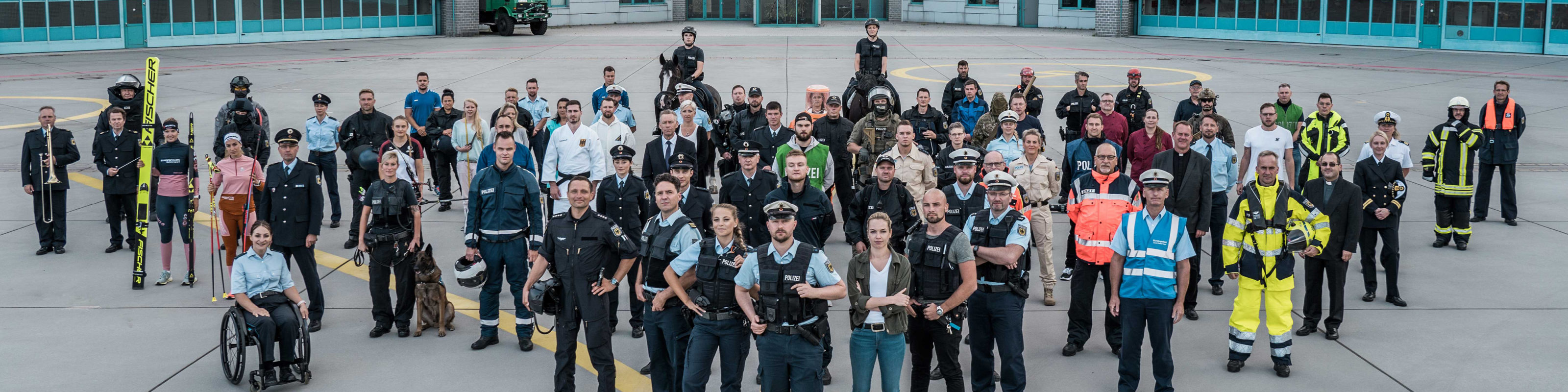 Gruppenbild verschiedener Bundespolizisten und Fachkräfte in verschiedenen Uniformen und Ausrüstungen, die auf einem großen Platz für den Einsatz bereitstehen. Text: 'Einsatzbereiche'.
