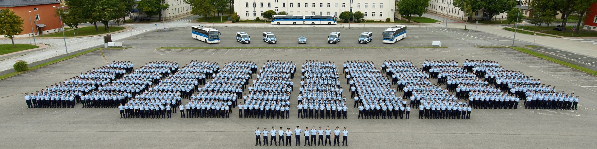 Luftaufnahme von mehreren Hundert Bundespolizei-Anwärtern in Uniform, die in einer Formation auf einem großen Platz stehen. Im Hintergrund sind mehrere Busse und Einsatzfahrzeuge zu sehen.