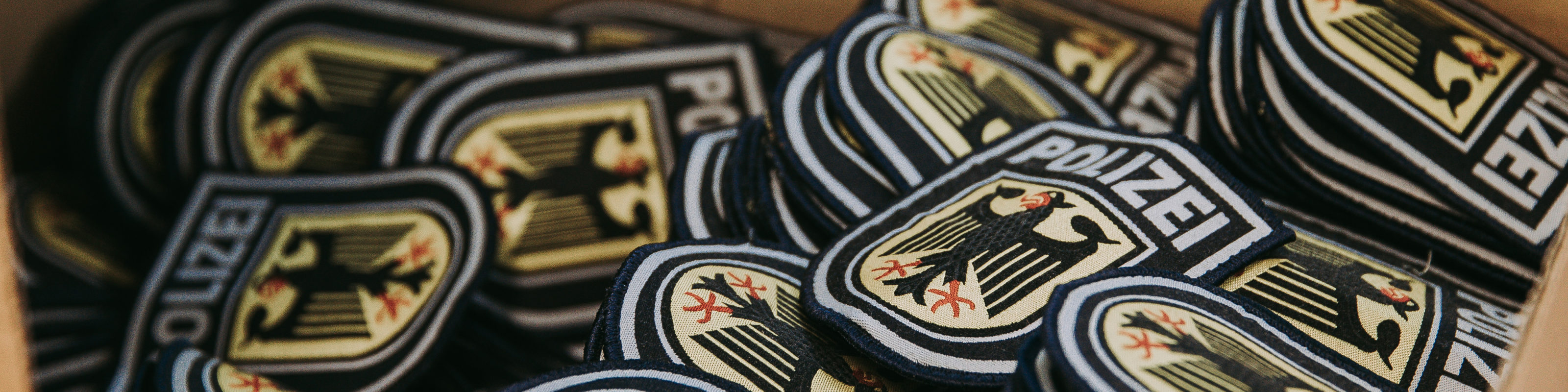 Headerbild der 'Über uns'-Seite der Bundespolizei-Website mit gestapelten Bundespolizei-Abzeichen, die das Bundeswappen und den Schriftzug 'Polizei' zeigen. Text auf dem Bild: 'Über uns'.